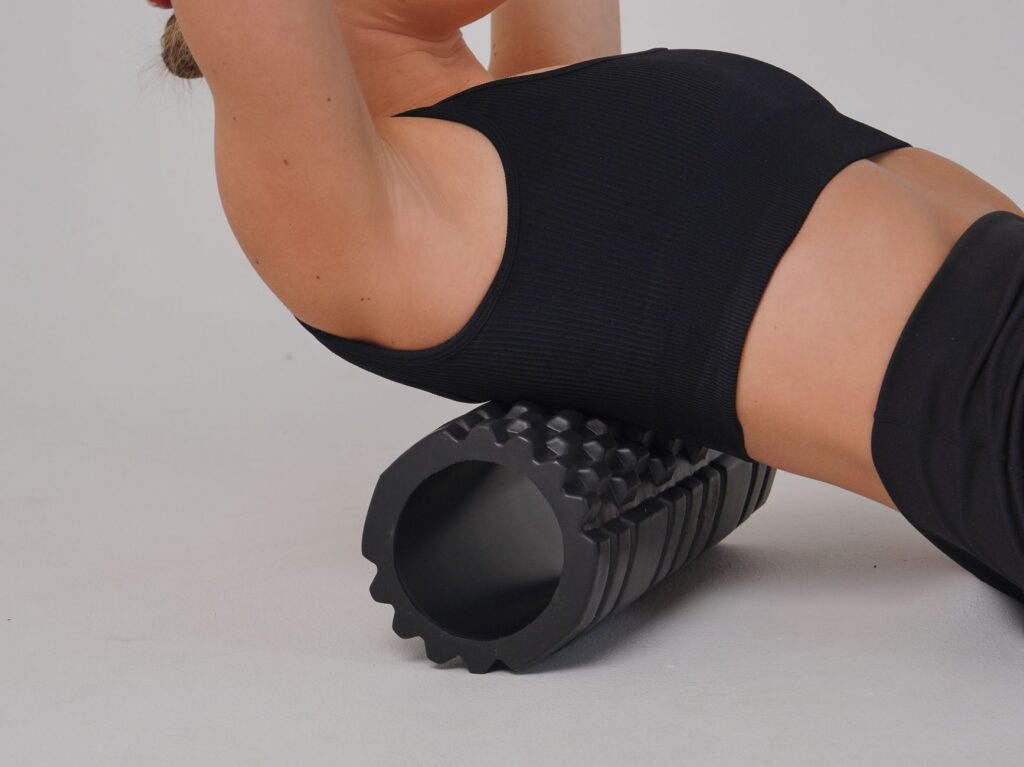 Frau massiert ihre Beinmuskulatur mit einer Faszienrolle auf einer Trainingsmatte