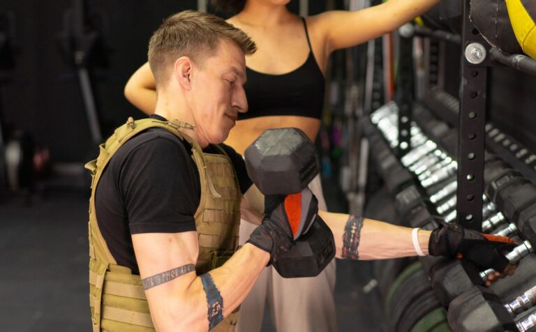 Mann mittleren Alters trainiert mit Gewichtsweste und Kurzhantel im Fitnessstudio