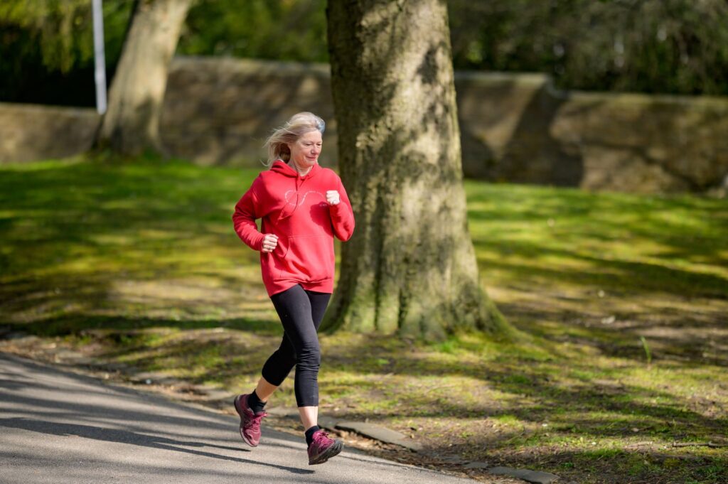 Läuferin mittleren Alters joggt entspannt auf einem Weg durch einen Park im Morgenlicht