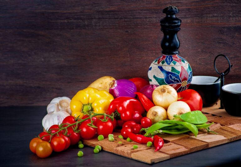 Frisches buntes Gemüse – Paprika, Tomaten, Zwiebeln und Knoblauch – auf einem rustikalen Holzbrett