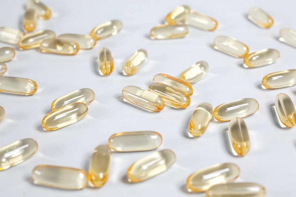 Goldgelbe Omega-3-Fischölkapseln liegen verstreut auf einer hellen Oberfläche