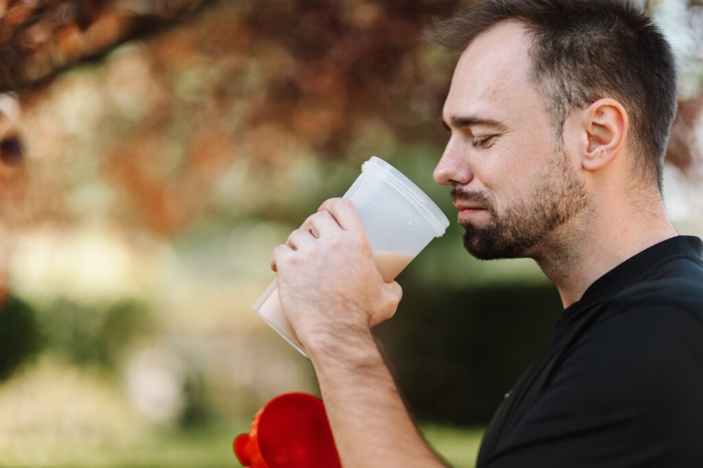 Ein Shaker mit Proteinpulver neben einem gehäuften Löffel auf der Küchentheke