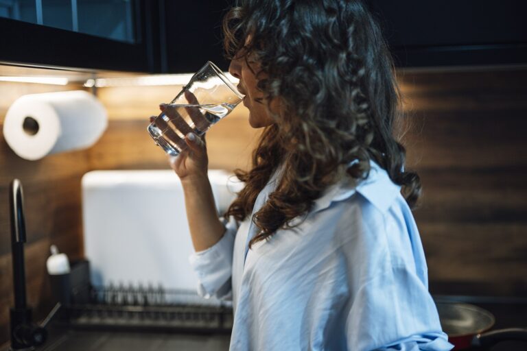Frau trinkt in einer modernen Küche Wasser aus einem Glas