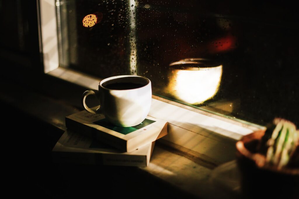 Dampfende Tasse Kaffee am Abend auf Büchern vor einem regennassen Fenster – Symbol für Koffein am Abend und Schlaf