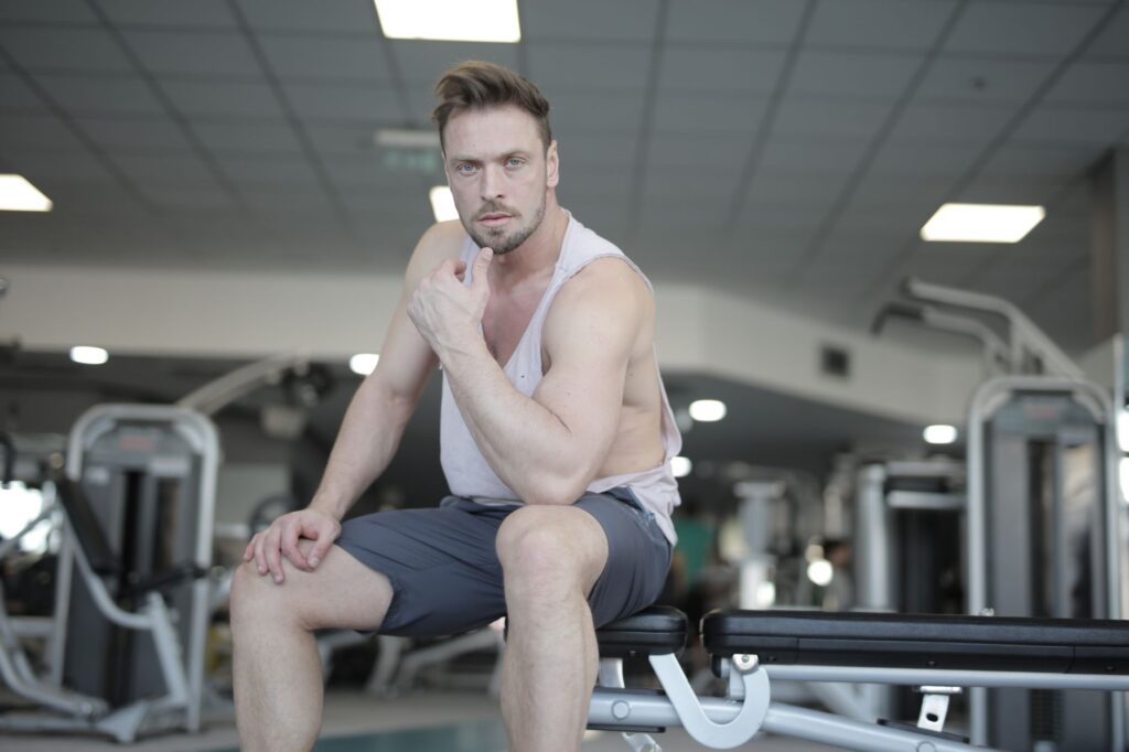 Mann sitzt nachdenklich auf einer Hantelbank im Fitnessstudio und macht eine Trainingspause