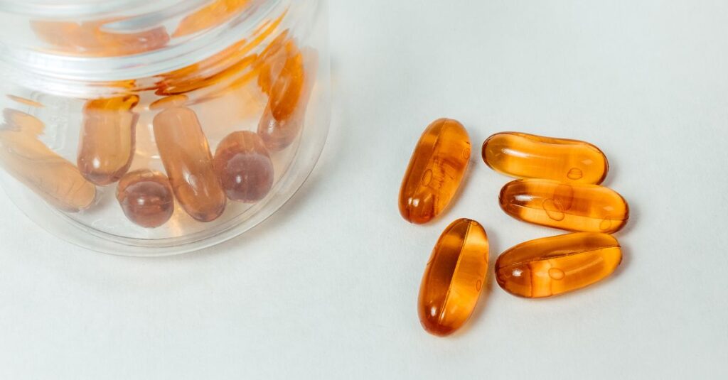Bernsteinfarbene Vitamin-Kapseln fallen aus einem Glasbehälter – Symbolbild für Nahrungsergänzung wie Vitamin K2