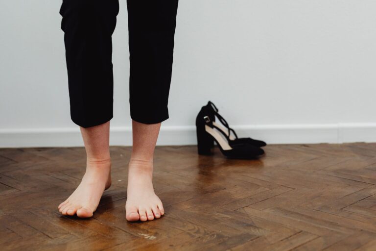 Barfüßige Person steht auf Parkettboden, die ausgezogenen Schuhe stehen daneben an der Wand
