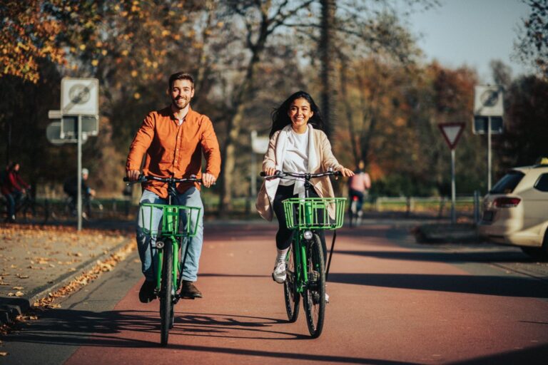Ein Mann und eine Frau fahren an einem sonnigen Herbsttag gemeinsam mit dem Fahrrad durch einen Park