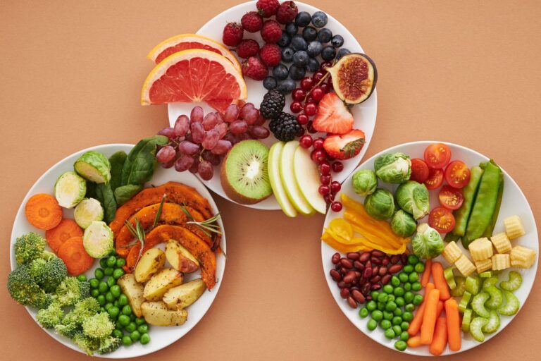 Drei weiße Teller von oben mit Gemüse, Beeren und Obst als Portionsbeispiele