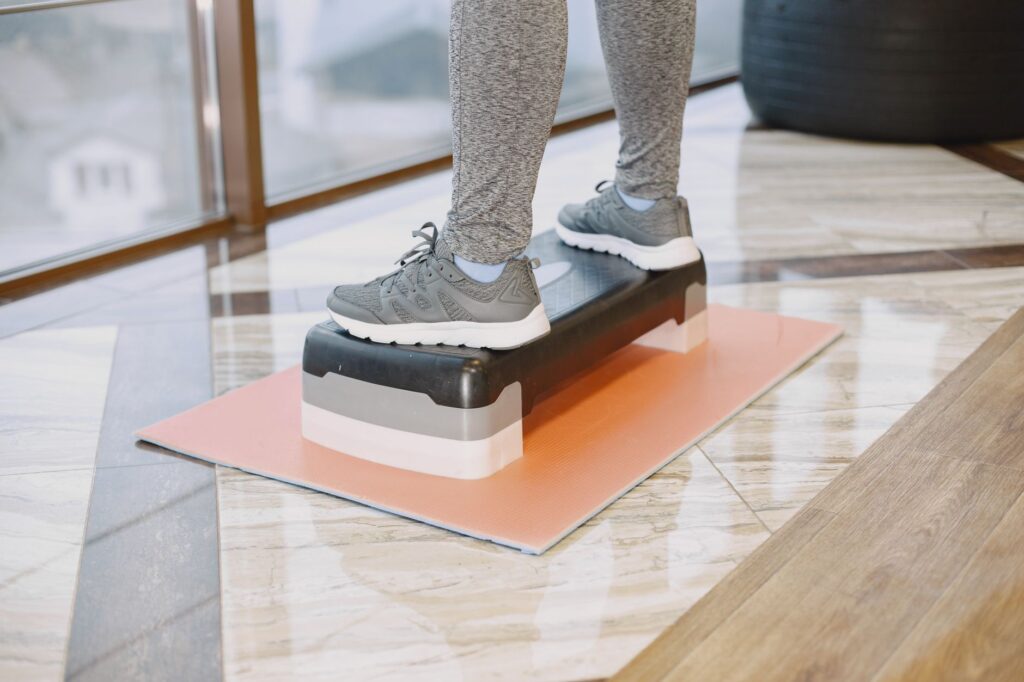 Fuesse in Sportschuhen auf einem Stepp-Brett auf einer Trainingsmatte im Wohnzimmer