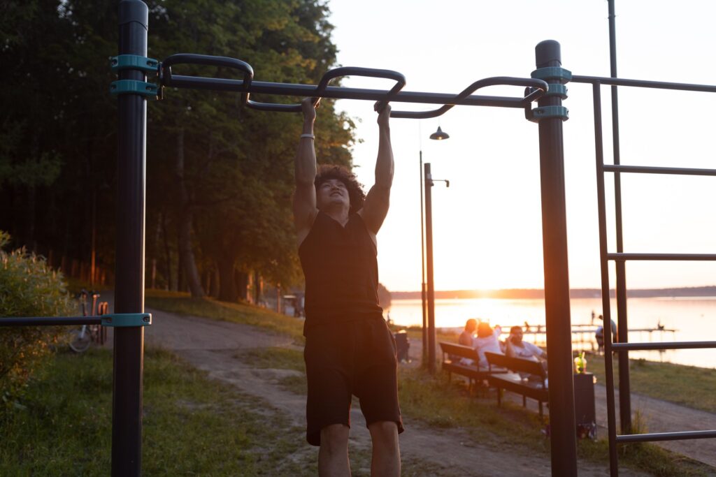 Mann trainiert bei Sonnenuntergang an Klimmzugstangen im Park am See