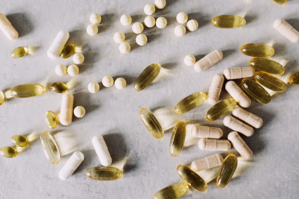 Verschiedene Nahrungsergaenzungskapseln und Tabletten flach ausgelegt auf hellem Marmoruntergrund