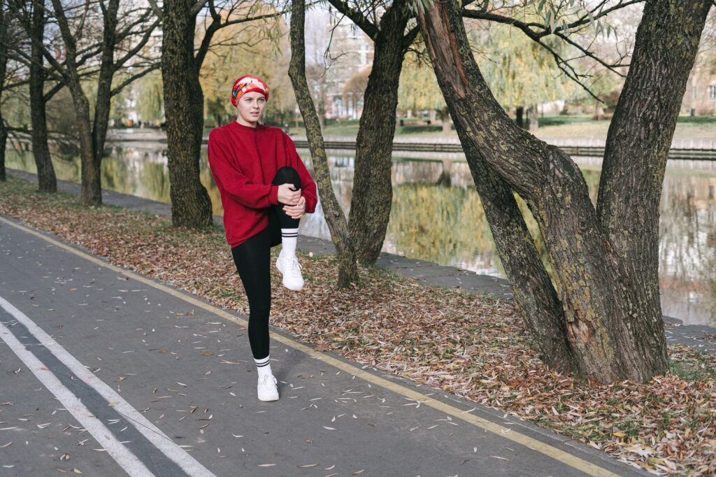 Frau im roten Pullover wärmt sich an einem herbstlichen Parkweg für einen Lauf auf