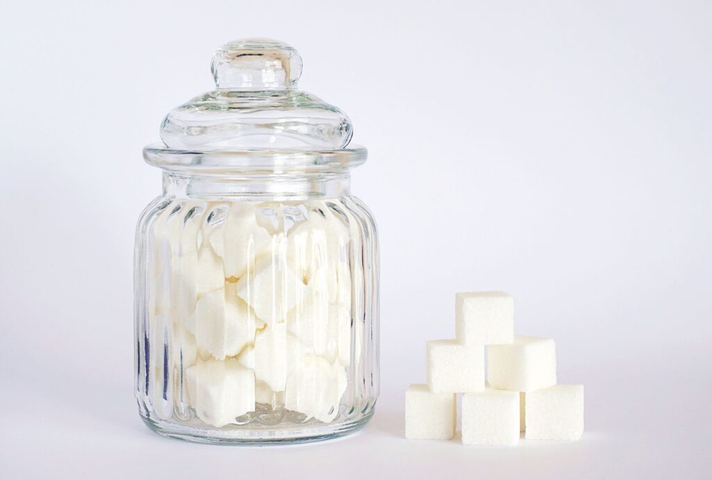 Glasgefäß voller Zuckerwürfel neben einem Stapel Würfelzucker – Symbolbild für Zucker und Süßstoff-Alternativen