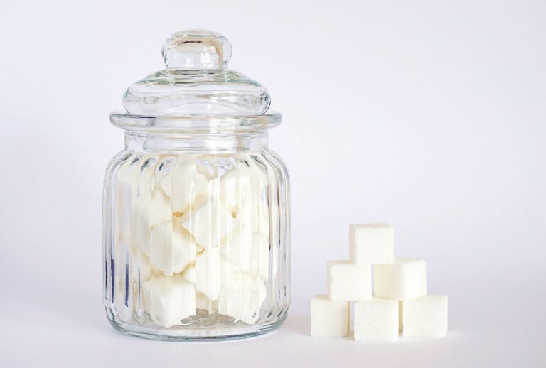 Glasgefäß voller Zuckerwürfel neben einem Stapel Würfelzucker – Symbolbild für Zucker und Süßstoff-Alternativen