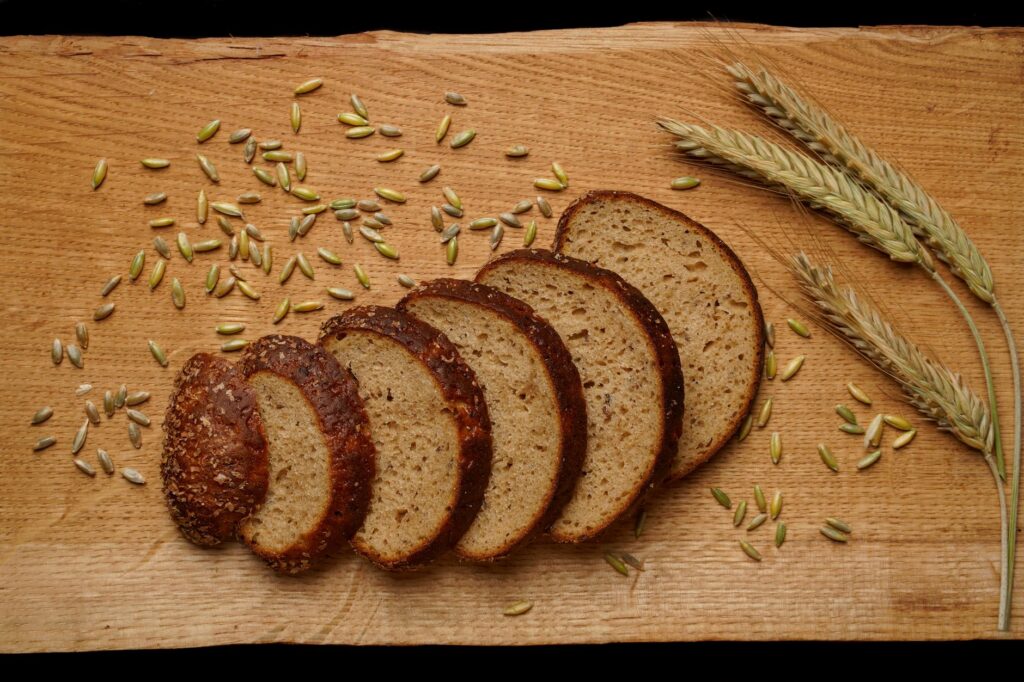 Aufgeschnittener dunkler Vollkornbrotlaib mit Roggenkörnern und Getreideähren auf einem Holzbrett