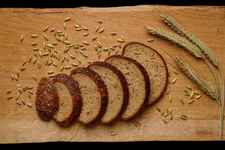 Aufgeschnittener dunkler Vollkornbrotlaib mit Roggenkörnern und Getreideähren auf einem Holzbrett