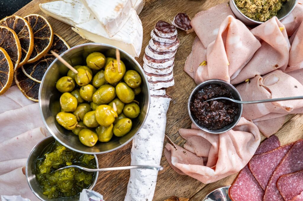 Holzbrett mit aufgeschnittener Salami, Schinken, Mortadella, Oliven und Käse von oben fotografiert