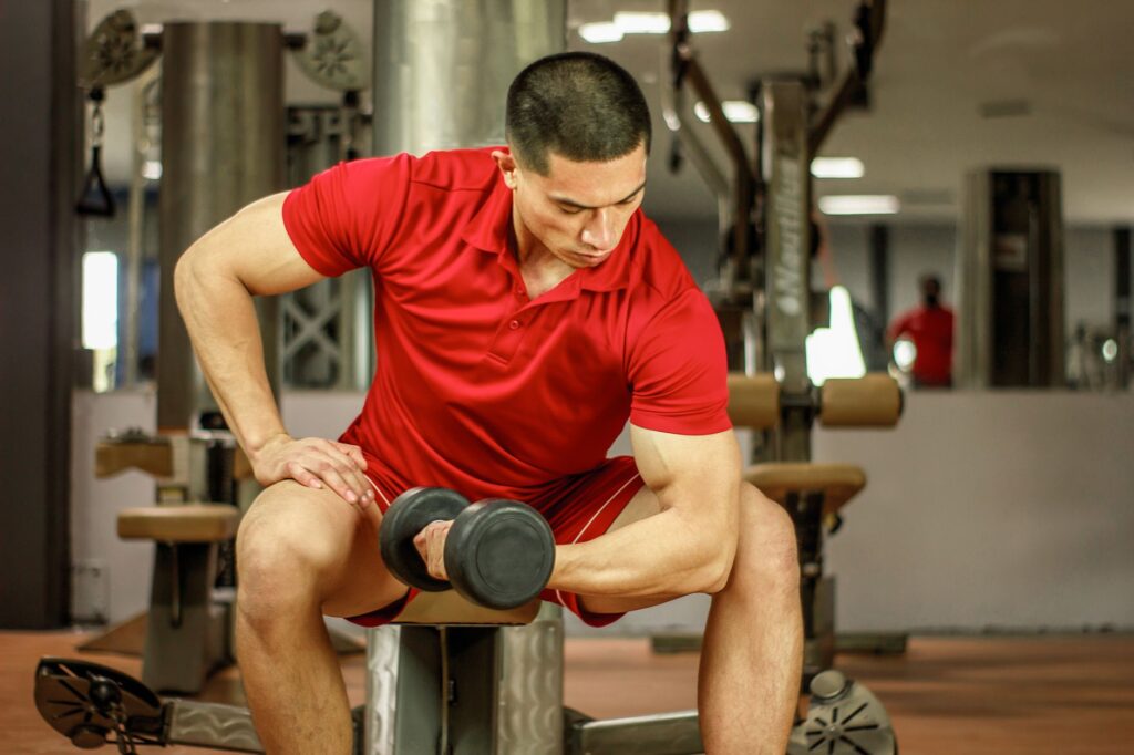 Mann im Fitnessstudio führt einen Konzentrations-Curl aus und senkt die Kurzhantel kontrolliert ab