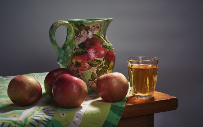 Glas Apfelsaft neben frischen Äpfeln und einem Krug auf einem Holztisch