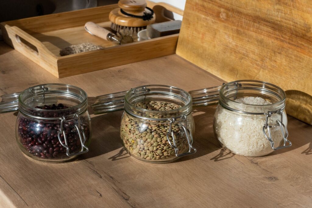 Hülsenfrüchte als Proteinquelle: Vorratsgläser mit roten Bohnen, grünen Linsen und Reis auf einem Holztisch