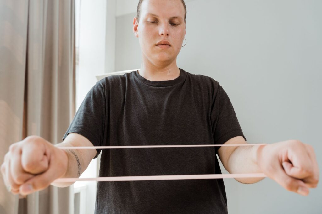 Person trainiert zu Hause im Wohnzimmer mit einem elastischen Widerstandsband auf Brusthöhe