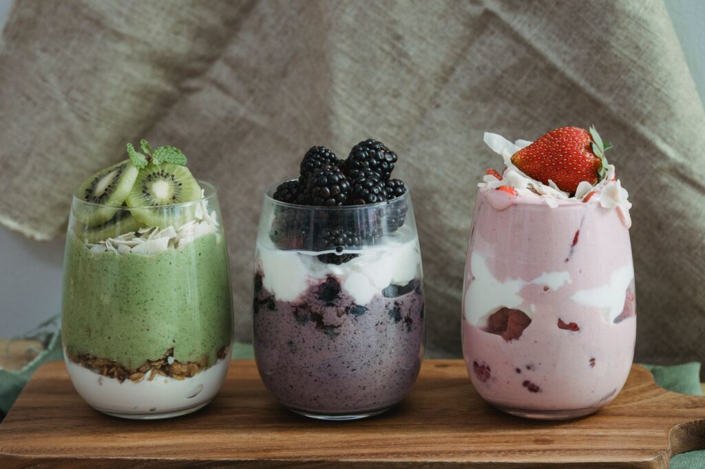 Drei Gläser mit Joghurt, Beeren und Müsli auf einem Holzbrett als proteinreiches Frühstück