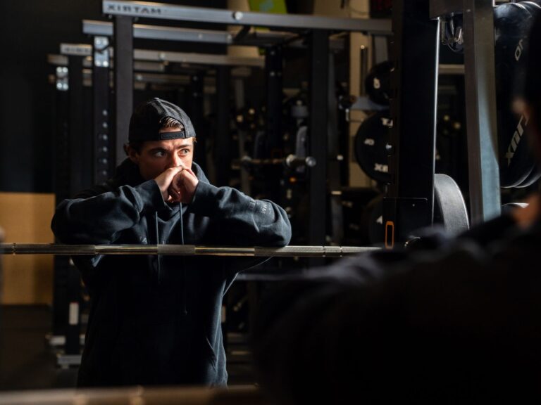 Mann stützt sich während der Satzpause an einer Langhantel im Power Rack