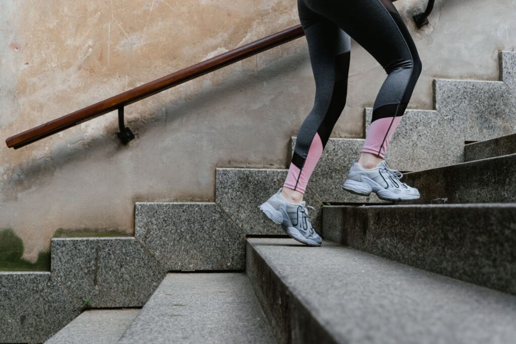 Frau in Sportleggings steigt zügig eine Steintreppe im Freien hinauf – Treppensteigen als Alltagstraining