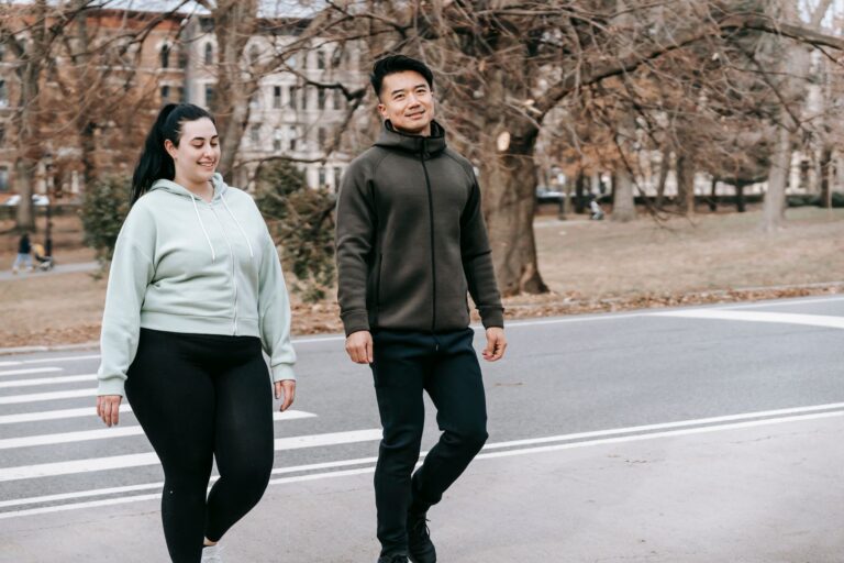 Zwei Menschen in Sportkleidung gehen zuegig ueber eine Strasse am Stadtpark