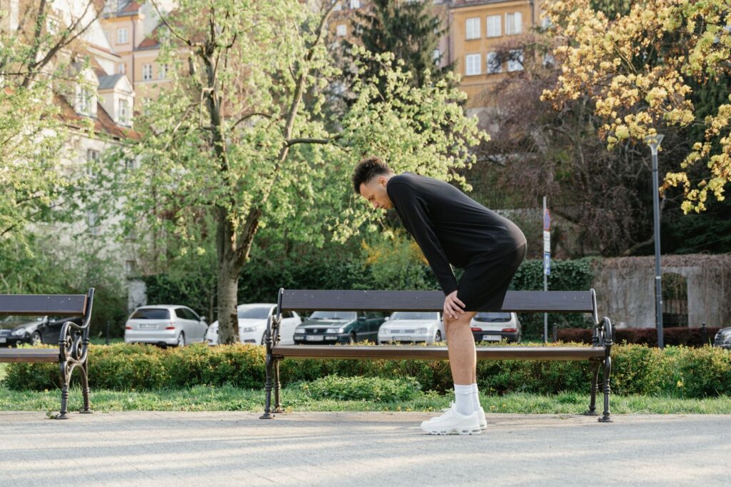 Sportlich gekleideter Mann steht nach dem Lauftraining im Park vorgebeugt und kommt wieder zu Atem