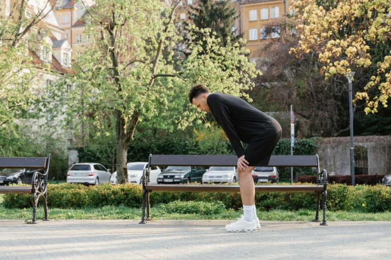 Sportlich gekleideter Mann steht nach dem Lauftraining im Park vorgebeugt und kommt wieder zu Atem