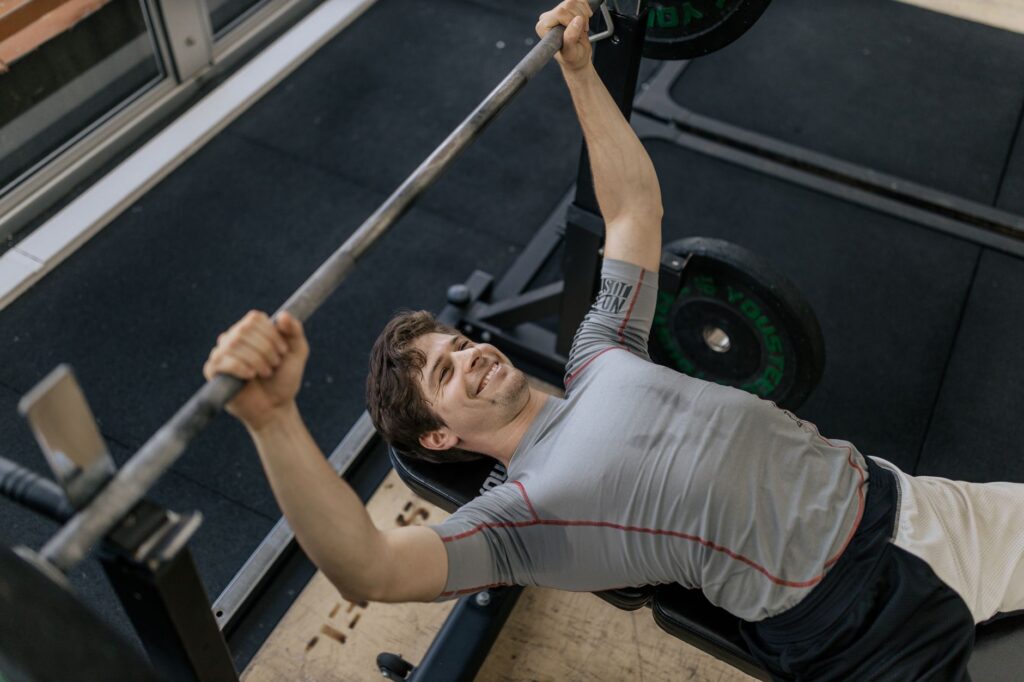 Mann beim Bankdrücken mit Langhantel im Fitnessstudio, sichtbare Anstrengung im letzten Satz