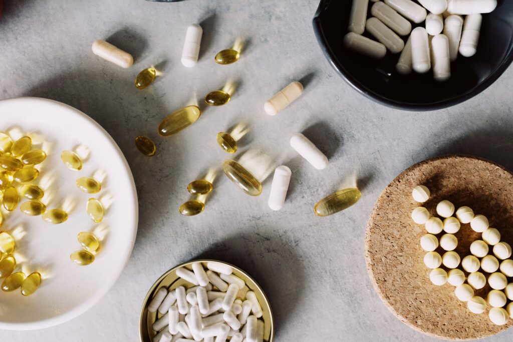 Verschiedene Nahrungsergänzungs-Kapseln und Tabletten in Schalen auf hellem Steinuntergrund, von oben fotografiert