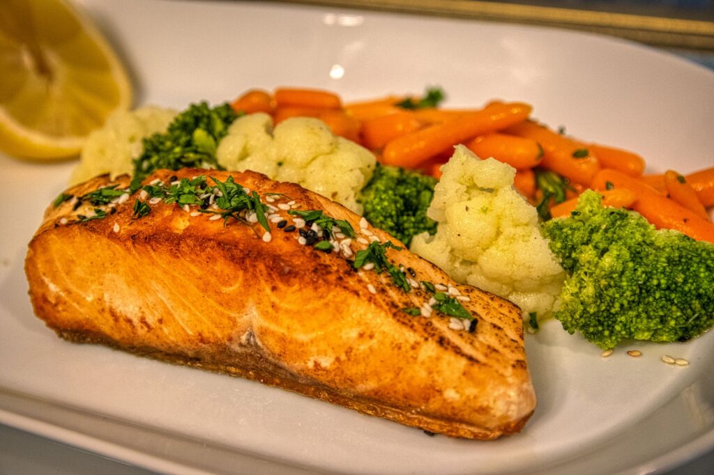 Gebratenes Lachsfilet mit Brokkoli, Karotten und Blumenkohl auf einem weißen Teller