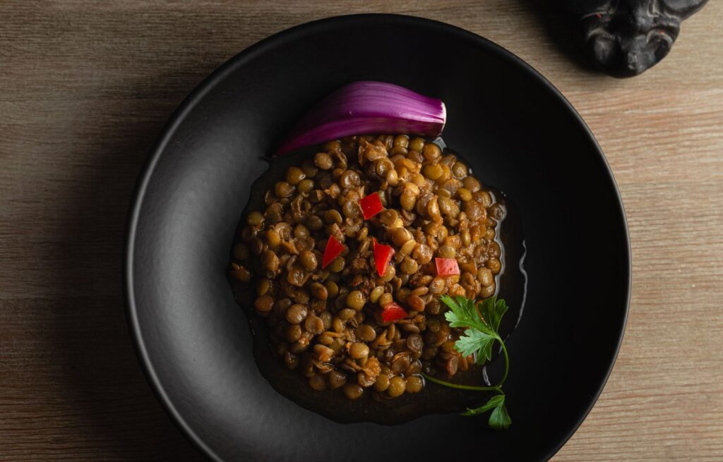 Schüssel mit gekochten Linsen, roter Zwiebel und Petersilie auf einem Holztisch
