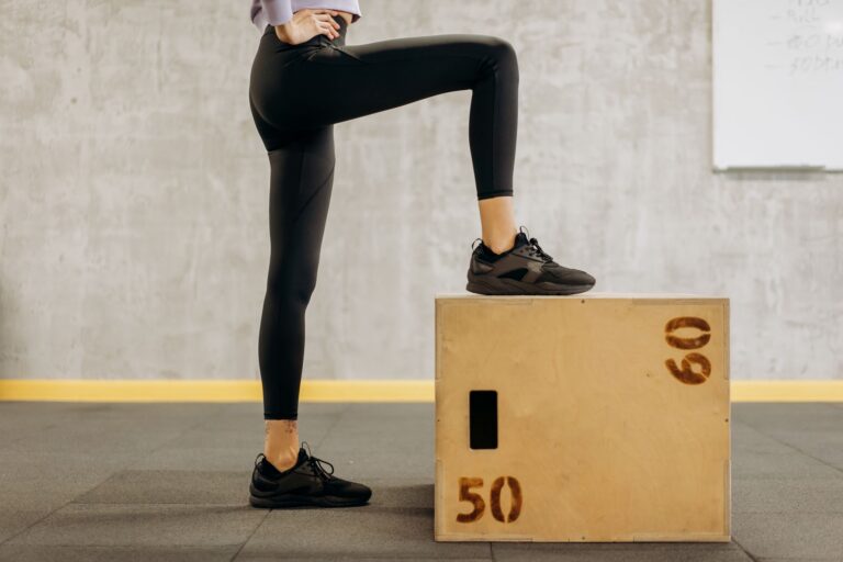 Frau setzt einen Fuß auf eine hölzerne Step-Up-Box im Trainingsraum – Ausgangsposition für Step-ups