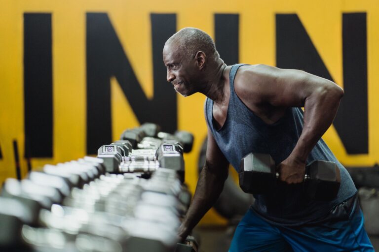 Mann mittleren Alters trainiert im Fitnessstudio mit einer Kurzhantel neben einem Hantelständer